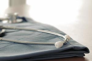Stethoskop mit blauem Arztkittel auf Holztisch mit flachem DOF, gleichmäßig abgestimmt und Hintergrund foto
