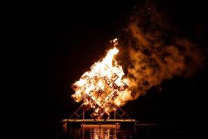 groß hölzern Struktur in Flammen Über Wasser beim Nacht foto