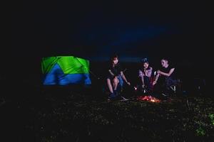 eine gruppe asiatischer freunde, die im sommer zusammen mit dem glück beim campen in der nähe des sees trinken und gitarre spielen foto