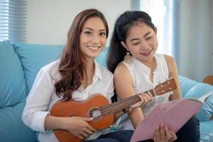 Zwei asiatische Frauen haben Spaß beim Ukulele spielen und lächeln zu Hause, um sich zu entspannen foto