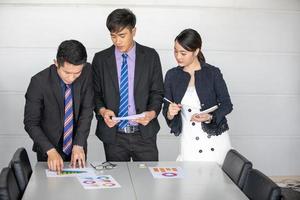 Geschäftsleute, die arbeiten und auf grafische Finanzdiagramme und Analysedokumente auf dem Bürotisch zeigen foto