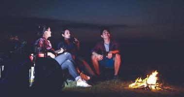 eine gruppe asiatischer freunde, die im sommer zusammen mit dem glück trinkt und gitarre spielt, während sie bei sonnenuntergang in der nähe des sees campen foto