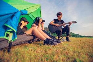 eine gruppe asiatischer freunde, die im sommer zusammen mit dem glück trinkt und gitarre spielt, während sie bei sonnenuntergang in der nähe des sees campen foto