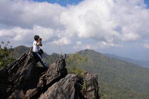 Frau sitzt auf Felsen mit Kamera, um im Sommer Bilder von Bergen aufzunehmen foto