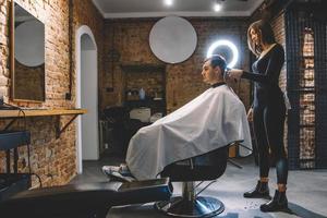 Schöne Friseurin, die die Haare des Kunden mit einer Schere in einem Friseursalon schneidet. konzept von werbung und friseur foto