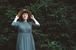 Frau mit Strohhut und Kleid mit geschlossenen Augen auf einem Hintergrund aus grünem Wald und Bäumen. Platz für Text oder Werbung foto