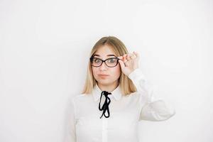 Porträt einer positiven schönen blonden Frau, die ein stilvolles weißes Hemd trägt, das ihre Brille auf einem weißen Hintergrund hält. kopieren, leerer platz für text foto