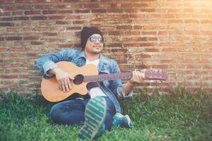 Hipster-Mann sitzt, während er Gitarre spielt und singt. foto