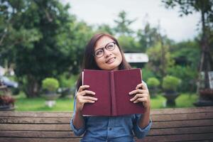 hipster charmantes mädchen, das etwas denkt, während es rotes buch im grünen park liest. foto