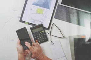 Draufsicht der Geschäftsmannhand, die mit Finanzen über Kosten und Taschenrechner und Laptop mit Mobiltelefon auf dem Schreibtisch im modernen Büro mit vr-Symboldiagramm arbeitet foto