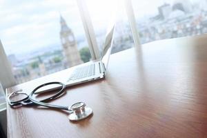 Stethoskop und Laptop-Computer auf Holztisch und London Bigben unscharfer Hintergrund kopieren Raum foto