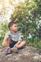 Trauriger kleiner Junge, der auf Felsen sitzt, im Park. foto