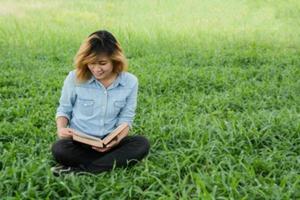 junge frau, die ein buch im park auf gras liest. foto