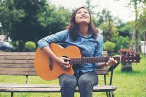 schöne junge frau, die gitarre spielt, sitzt auf einer bank, glückliches zeitkonzept. foto