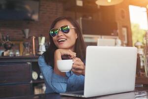 hübsche junge hipster-frau, die mit ihrem laptop in einem café sitzt, wegschaut und glücklich lächelt, sich mit urlaub entspannt, frauen-lifestyle-konzept. foto