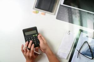 Draufsicht der Geschäftsmannhand, die mit Finanzen über Kosten und Taschenrechner und Laptop mit Handy auf dem Schreibtisch im modernen Büro arbeitet foto