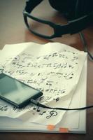 Closeup-Buchse des Smartphones mit Kopfhörer auf Musiknotenpapier mit flachem DOF, das gleichmäßig auf dem Holzschreibtisch abgestimmt ist foto