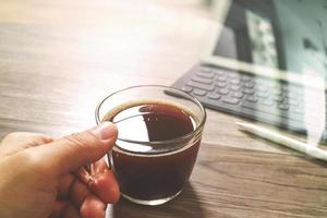 Hand mit Kaffeetasse oder Tee und digitaler Tischdock-Smart-Tastatur, Stylus-Stift auf Holztisch, Filtereffekt foto