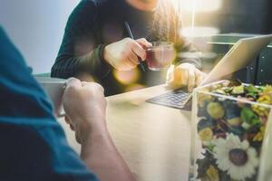 Kaffeepause im Büro mit zwei Designerkollegen, die sich bei Kaffeetassen unterhalten, Blumenvase, digitales Tablet, das intelligente Tastatur auf Marmorschreibtisch andockt, Film mit Filtereffekt foto