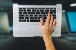 Draufsicht des Geschäftsmannes, der Tastatur mit Laptop-Computer auf hölzernem Schreibtisch im modernen Büro tippt foto