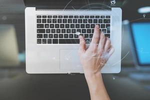 Draufsicht des Geschäftsmannes, der Tastatur mit Laptop-Computer auf hölzernem Schreibtisch im modernen Büro mit Ikonendiagramm der virtuellen Realität tippt foto