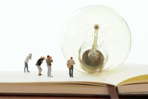 kreatives Ideenkonzept - Miniaturfotograf mit Vintage-Glühbirne auf offenem Papiernotizbuch foto