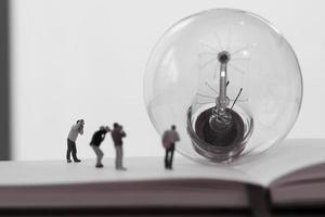 kreatives Ideenkonzept - Miniaturfotograf mit Vintage-Glühbirne auf offenem Papiernotizbuch foto