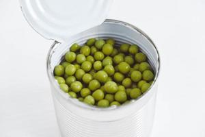 Konservierte grüne Zuckererbsen in einer offenen Aluminiummetalldose auf einem weißen Tisch. Ansicht von oben. kopieren, leerer platz für text foto