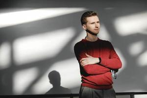 junger Mann in einem roten Pullover auf weißem Hintergrund mit Schatten aus dem Licht. kopieren, leerer platz für text foto
