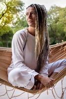 blonde Yogi-Frau mit Dreadlocks, die in einer gewebten Hängematte sitzt. foto