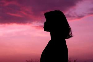 Silhouette mittlerer Schuss einer Frau oder einer Frau, die mit dem Himmelsuntergangshintergrund auf der Sonnenuntergangszeit steht. foto