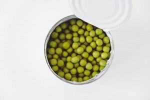 Konservierte grüne Zuckererbsen in einer offenen Aluminiummetalldose auf einem weißen Tisch. Ansicht von oben. kopieren, leerer platz für text foto