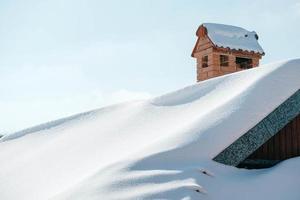schneebedecktes Dach und Schornstein aus rotem Backstein im Hintergrund des blauen Himmels. kopieren, leerer platz für text foto
