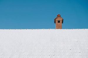 schneebedecktes Dach und Schornstein aus rotem Backstein im Hintergrund des blauen Himmels. kopieren, leerer platz für text foto