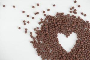 Schokoladenmaiskugeln verstreut in Form eines Herzens auf weißem Hintergrund. Ansicht von oben. kopieren, leerer platz für text foto