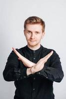 Porträt eines jungen Mannes in einem schwarzen Hemd zeigt ein Verbotsschild mit seinen Händen auf weißem Hintergrund. kopieren, leerer platz für text foto