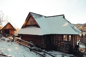Holzhaus bei Sonnenuntergang auf dem Hintergrund schneebedeckter Berge. Winterlandschaft in den Karpaten. ukraine, europa. kopieren, leerer platz für text foto