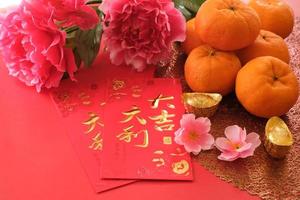 chinesisches neujahrsfestkonzept. Mandarinen, rote Umschläge und Goldbarren auf rotem Grund, verziert mit Pflaumenblüte. chinesisches schriftzeichen da ji da li bedeutet großes glück großer gewinn. foto