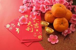 chinesisches neujahrsfestkonzept. Mandarinen, rote Umschläge und Goldbarren auf rotem Grund, verziert mit Pflaumenblüte. chinesisches schriftzeichen da ji da li bedeutet großes glück großer gewinn. foto