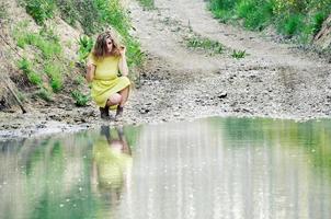 Schönes blondes Mädchen, gekleidet mit einem grünen Kleid, in der Nähe eines Sees foto