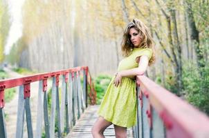 Schönes blondes Mädchen, gekleidet mit einem beigen Kleid, das in einer ländlichen Brücke steht foto