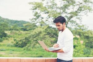 Hipster-Mann mit Laptop, der draußen in Natur, Freiheit und Glückskonzept steht foto