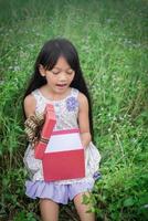 kleines Mädchen, das mit einem Geschenk am Feld sitzt und es so überrascht ansieht foto
