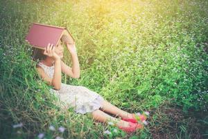kleines süßes asiatisches Mädchen-Cover-Buch auf dem Kopf in der Natur. foto