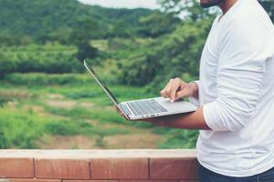 Hipster-Mann mit Laptop, der draußen in Natur, Freiheit und Glückskonzept steht foto