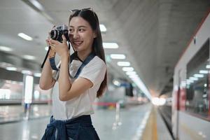 Eine junge schöne asiatische Touristin, Fotografin, die Schnappschüsse mit Filmkamera macht, Lächeln und Freude am Bahnsteig, glücklicher Reiselebensstil mit der U-Bahn-Urlaubsreise. foto