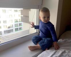 schönes Baby mit Kindergesicht posiert Fotograf in der Nähe von Fenster foto