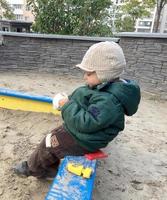 schönes Baby im Kindersandkasten posiert Fotograf in der Nähe von Sandkasten foto