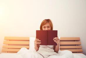 Schöne junge Frau, die auf dem Bett schläft, nachdem sie ein Buch gelesen hat, dessen Gesicht vom Buch bedeckt ist foto