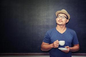 Gutaussehender Mann mit einer Tasse Kaffee, der vor der Tafel steht und etwas denkt foto